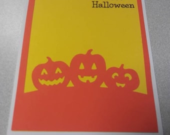 May include: A Halloween greeting card with a white border. The card features a yellow background with the words "Happy Halloween" in black. Below the text are three orange jack-o'-lanterns.