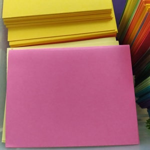 May include: A collection of colorful paper sheets, including stacks of yellow, pink, and a rainbow of other hues. The sheets are neatly arranged, suggesting a stationery or craft supply theme.