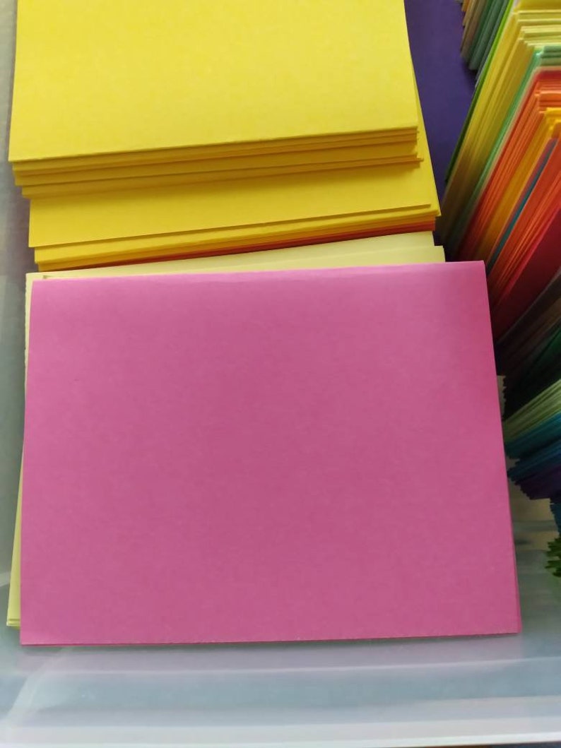 May include: A collection of colorful paper sheets, including stacks of yellow, pink, and a rainbow of other hues. The sheets are neatly arranged, suggesting a stationery or craft supply theme.