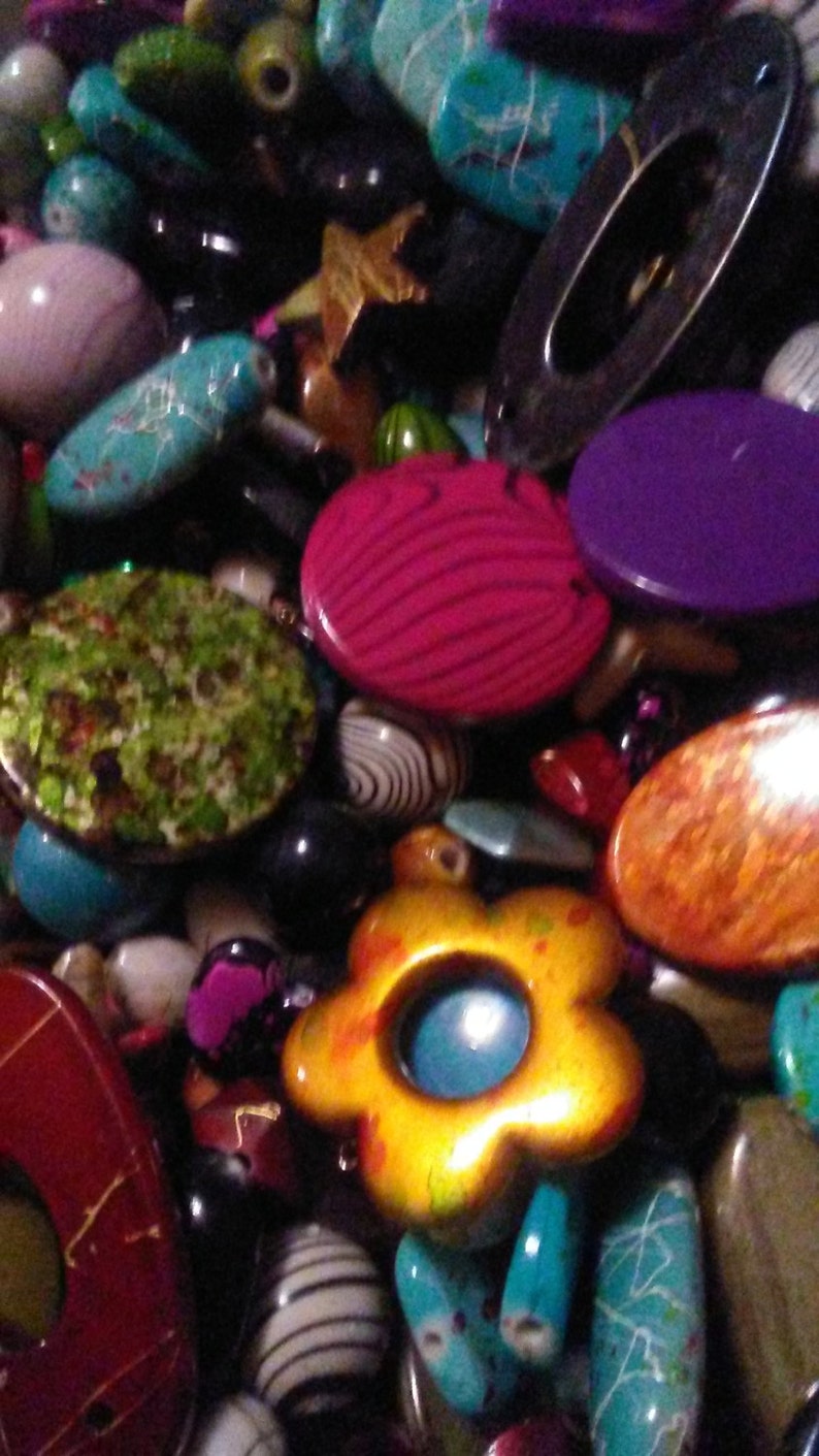 May include: A close-up of a collection of beads and decorative items. The image features a variety of shapes and colours, including turquoise, pink, purple, and yellow. Some beads have patterns, such as stripes and floral designs, creating a diverse and visually appealing mix.