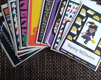 May include: A collection of Halloween greeting cards with various designs, including bats, pumpkins, and a witch on a broom. The cards feature black, white, orange, purple, and yellow colors. One card reads "Happy Halloween".