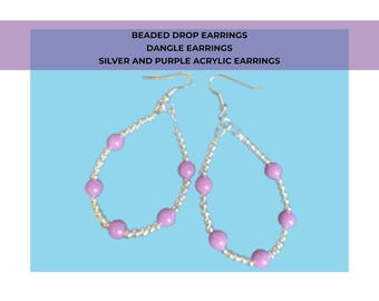 May include: A pair of silver-toned beaded drop earrings with purple acrylic beads. The earrings are teardrop-shaped and hang from silver hooks. The text in the image reads: "BEADED DROP EARRINGS, DANGLE EARRINGS, SILVER AND PURPLE ACRYLIC EARRINGS."
