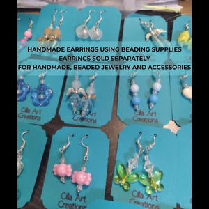 May include: A selection of handmade earrings on teal cards. The earrings showcase diverse designs, such as beaded, floral, and butterfly motifs. The cards display the text "HANDMADE EARRINGS USING BEADING SUPPLIES" and "Cilla Art Creations."