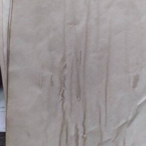 K&ouml;nnte beinhalten: Ein Stapel gealterter, cremefarbener Papierb&ouml;gen. Das Papier hat ein strukturiertes Aussehen mit vertikalen Streifen in einem dunkleren, br&auml;unlichen Farbton, was auf Wassersch&auml;den oder Flecken hindeutet. Die R&auml;nder des Papiers weisen leichte Verf&auml;rbungen auf.