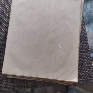 K&ouml;nnte beinhalten: Ein Stapel gealterter, cremefarbener Papierbl&auml;tter. Das Papier hat eine leicht strukturierte Oberfl&auml;che und weist Gebrauchsspuren auf, mit subtilen Verf&auml;rbungen und Knitterfalten. Die Kanten des Papiers sind sichtbar, was auf einen betr&auml;chtlichen Stapel hindeutet.