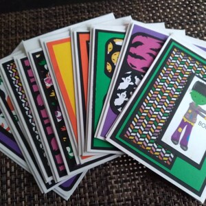 May include: A collection of Halloween-themed greeting cards. Each card features a unique design with vibrant colors, including images of ghosts, pumpkins, and Frankenstein's monster. The cards have a white border and are arranged in a fan shape.