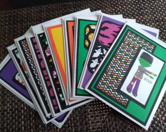 May include: A collection of Halloween-themed greeting cards. Each card features a unique design with vibrant colors, including images of ghosts, pumpkins, and Frankenstein's monster. The cards have a white border and are arranged in a fan shape.