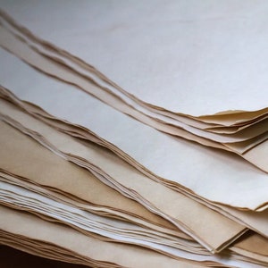 K&ouml;nnte beinhalten: Ein Stapel gealterter Papierb&ouml;gen mit unregelm&auml;&szlig;igen, gerissenen Kanten. Das Papier hat einen warmen, cremefarbenen Farbton mit dunkleren, br&auml;unlichen R&auml;ndern, was einen Vintage-Look erzeugt. Die Bl&auml;tter sind geschichtet und erzeugen einen strukturierten visuellen Effekt.