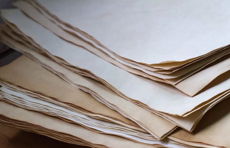 K&ouml;nnte beinhalten: Ein Stapel gealterter Papierb&ouml;gen mit unregelm&auml;&szlig;igen, gerissenen Kanten. Das Papier hat einen warmen, cremefarbenen Farbton mit dunkleren, br&auml;unlichen R&auml;ndern, was einen Vintage-Look erzeugt. Die Bl&auml;tter sind geschichtet und erzeugen einen strukturierten visuellen Effekt.