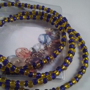May include: A beaded necklace featuring alternating gold and dark blue beads. The necklace is made of small, round beads strung together, creating a layered effect. The necklace is displayed on a white surface.