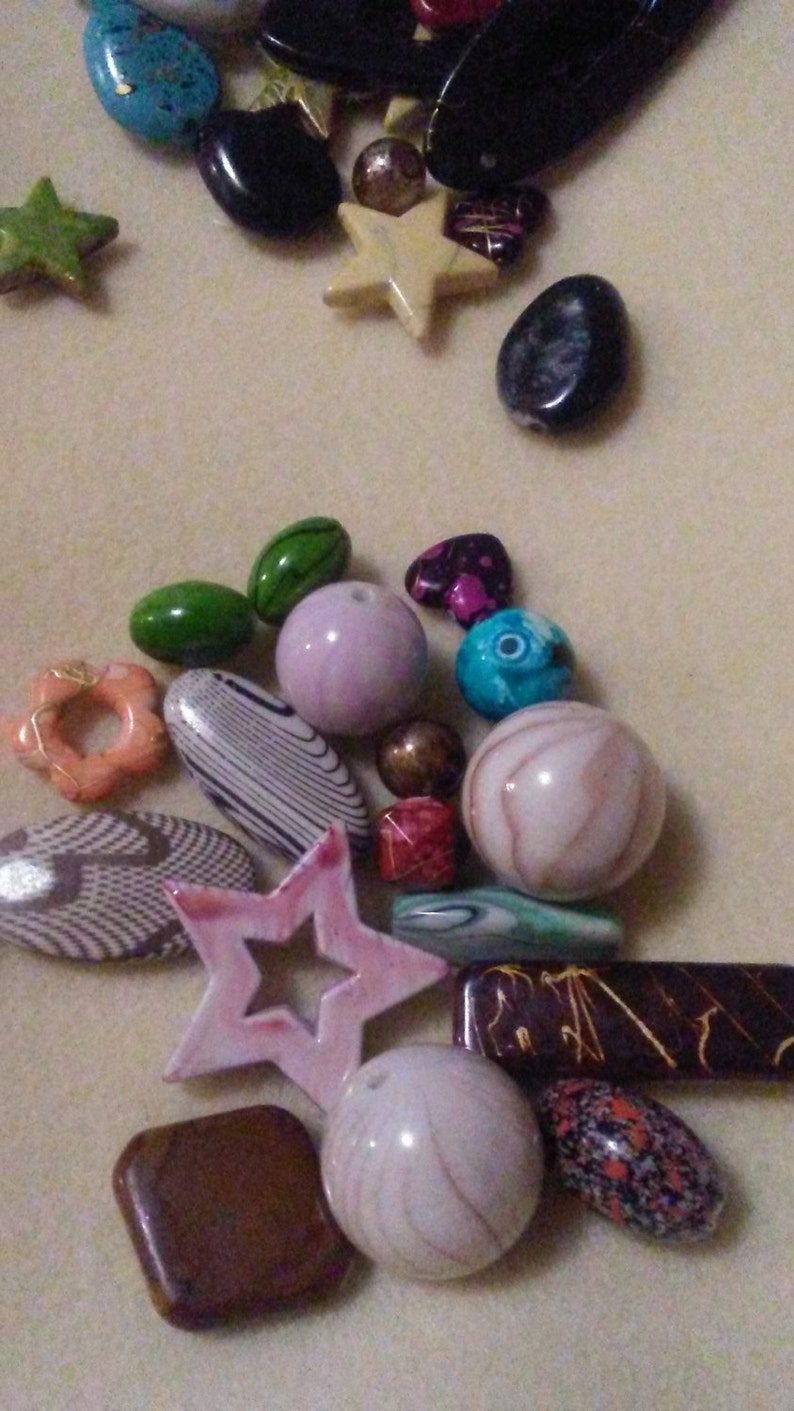 May include: A collection of colourful beads in diverse shapes and sizes. Includes green, pink, blue, and brown beads, along with star and oval shapes. Some beads have unique patterns and textures, suitable for jewellery making.