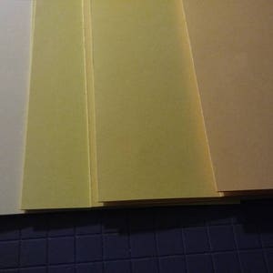 May include: A stack of rectangular sheets of paper in varying shades of yellow and tan. The colors range from a pale cream to a deeper, golden hue. The papers are neatly arranged, suggesting a stationery or craft supply.
