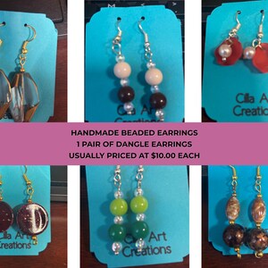 May include: Handmade beaded dangle earrings in various designs. The earrings feature gold-tone hooks and a variety of beads in colors like clear, brown, red, green, and brown. Each pair is displayed on a blue card with the text "Cilla Art Creations".