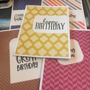 Könnte beinhalten: Eine Sammlung handgefertigter Grußkarten mit verschiedenen Mustern, darunter gelbe Vierpass-Formen, rosa Zickzacklinien und braune Punkte. Jede Karte zeigt den Text "happy BIRTHDAY" in schwarzer Tinte auf einem weißen Etikett mit abgerundeten Ecken.