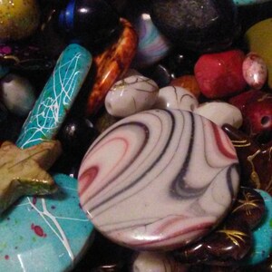 May include: A selection of colourful beads in various shapes and sizes. The beads include oval, round, and star-shaped designs, with colours like turquoise, red, black, and white. Some beads have intricate patterns.