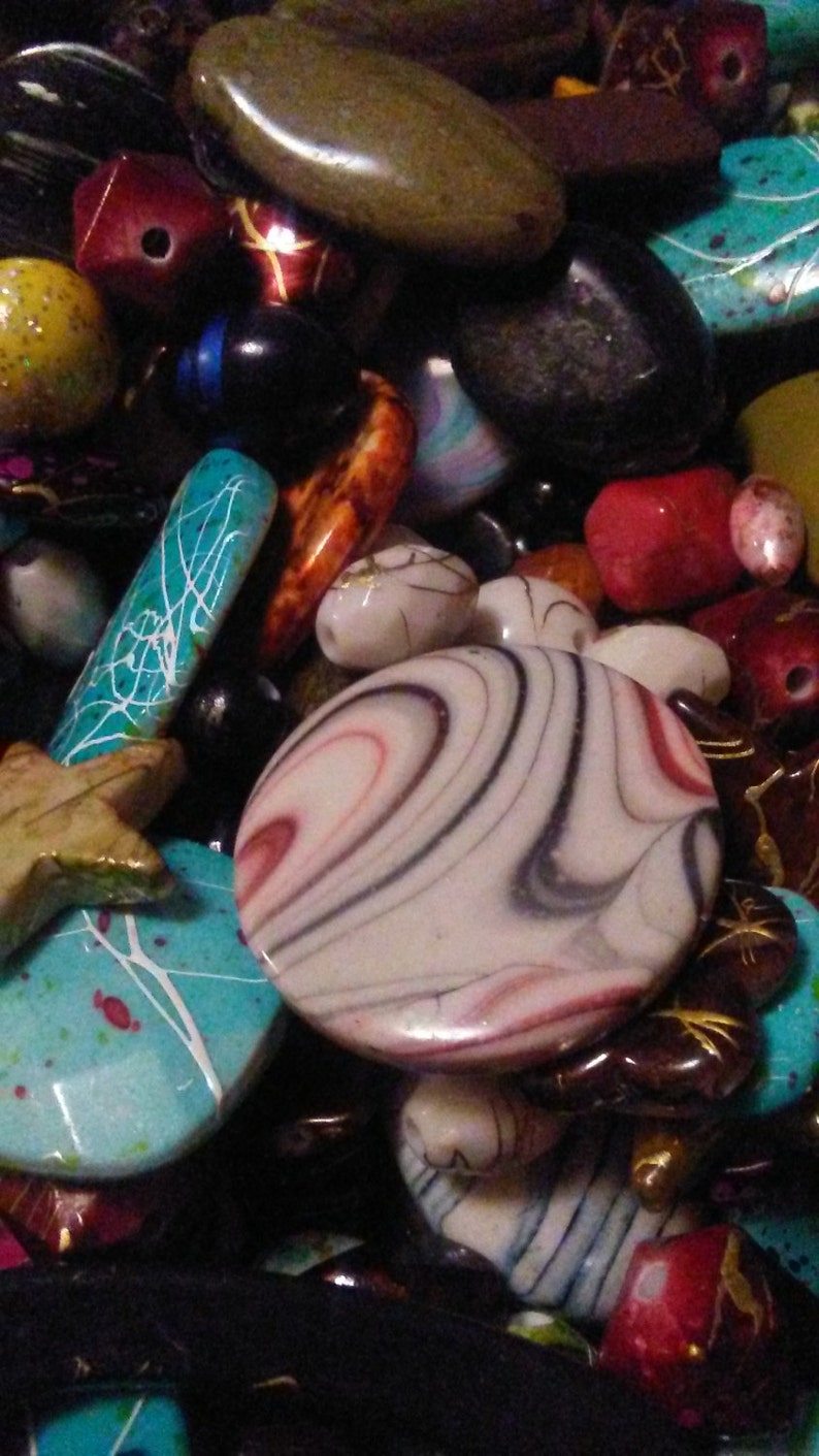 May include: A selection of colourful beads in various shapes and sizes. The beads include oval, round, and star-shaped designs, with colours like turquoise, red, black, and white. Some beads have intricate patterns.