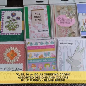 Könnte beinhalten: Verschiedene A2-Grußkarten in Klarsichtverpackungen. Die Designs umfassen Blumen-, Baby- und Feiertagsmotive. Die Karten haben verschiedene Farben und Muster, mit Texten wie "Celebrate you today" und "Welcome baby".