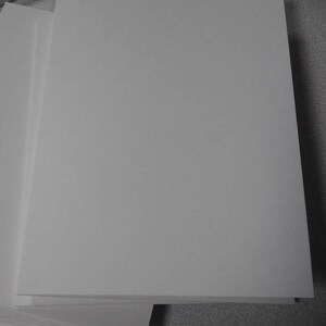 Op de afbeelding: Een stapel witte, blanco papieren vellen, waarschijnlijk voor printen of schrijven. Het papier is glad en rechthoekig, met een schoon, helder uiterlijk. De afbeelding toont een close-up van het papier, waarbij de textuur en randen worden benadrukt. Het papier ligt op een grijze ondergrond.