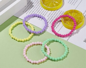 May include: A collection of colorful beaded bracelets in pastel shades of yellow, purple, pink, and green. The bracelets are arranged on a light green surface with lemon slices and text in the background.