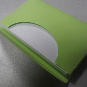 K&ouml;nnte beinhalten: Eine hellgr&uuml;ne CD-H&uuml;lle aus Papier mit einer teilweise sichtbaren wei&szlig;en CD. Die H&uuml;lle ist ge&ouml;ffnet und gibt die Disc frei. Die H&uuml;lle liegt auf einer grauen Oberfl&auml;che.