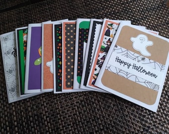 May include: A collection of Halloween greeting cards with various designs. The cards feature images of ghosts, spiders, witches, and patterns like polka dots and stars. The words "Happy Halloween" are written on one card.