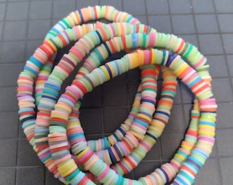May include: A collection of colorful, flat disc beads strung together to form multiple strands. The beads are arranged in a circular pattern, showcasing a variety of pastel and vibrant colors, including pink, green, yellow, and blue. The beads appear to be made of a lightweight material.