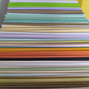 May include: A stack of colorful paper sheets in various hues, including red, orange, green, and purple. The paper is neatly arranged, creating a visually appealing display of stationery supplies. The image showcases a variety of colors and textures.