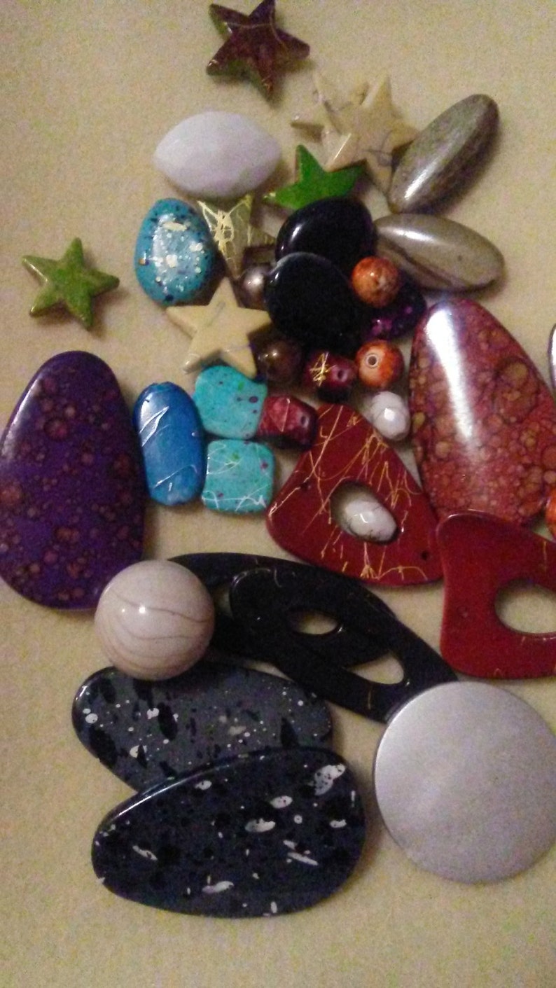 May include: A selection of beads and decorative items in various shapes. Includes star, oval, and irregular forms in colours such as purple, red, black, blue, and white. Some pieces feature speckled or patterned designs.