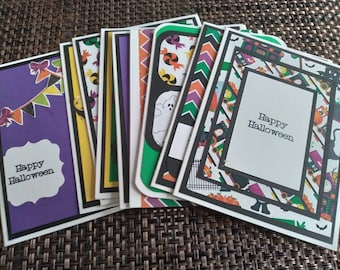May include: A collection of handmade Halloween greeting cards. Each card features a unique design with festive colors like purple, orange, and black. The cards have the text "Happy Halloween" on them. The cards are layered with decorative borders and patterns.