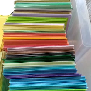 May include: A stack of colorful cardstock paper in various shades, including green, yellow, orange, blue, and purple. The paper is neatly arranged, creating a vibrant and organized display. Ideal for crafting and stationery projects.