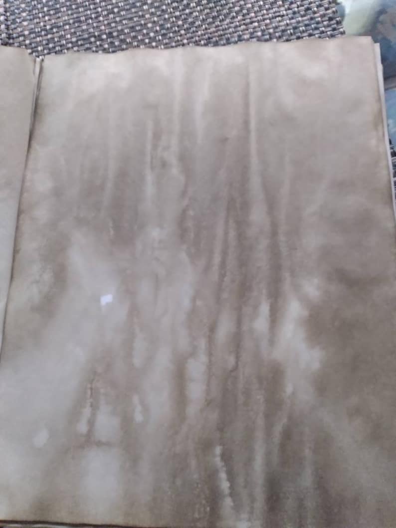 K&ouml;nnte beinhalten: Offene Buchseiten mit einem fleckigen, gealterten Aussehen. Das Papier hat eine gesprenkelte, braune und beige Farbe mit dunkleren Streifen und Flecken, was auf eine Vintage- oder Antik-&Auml;sthetik hindeutet. Die Textur erscheint leicht rau.
