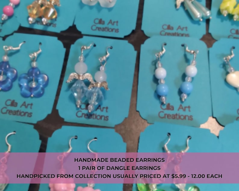 May include: A collection of handmade beaded dangle earrings displayed on teal cards. The earrings feature various designs, including flower shapes, angel figures, and beaded strands in shades of blue, white, and clear. Each pair is unique.
