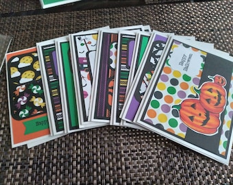 May include: A collection of handmade Halloween greeting cards. The cards feature various designs, including pumpkins, candy, and patterns in orange, black, green, and purple. Some cards have the text "Happy Halloween".