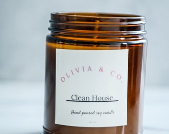 May include: A brown glass jar candle with a white label that reads "Olivia & Co. Clean House Hand poured soy candle".