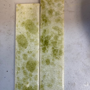 May include: Two rectangular ceramic tiles with a white background and green abstract patterns. The tiles have a crackled glaze.