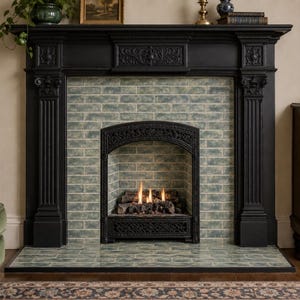 May include: A black fireplace mantel with ornate carved details and fluted columns surrounding a firebox. The interior and hearth are lined with rectangular, variegated blue-green subway tiles. A gas fire burns with small flames over logs.