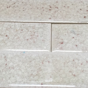 May include: White ceramic tile with a crackled glaze and small red flecks throughout. The tile has a smooth, glossy finish.
