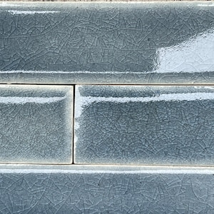 May include: Three rectangular ceramic tiles with a light blue glaze and a crackled finish. The tiles have a white border.