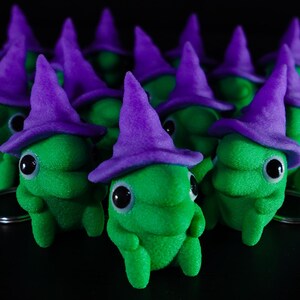 May include: A group of green witch figurines with purple hats and big eyes. The figurines are arranged in a semi-circle on a black surface.