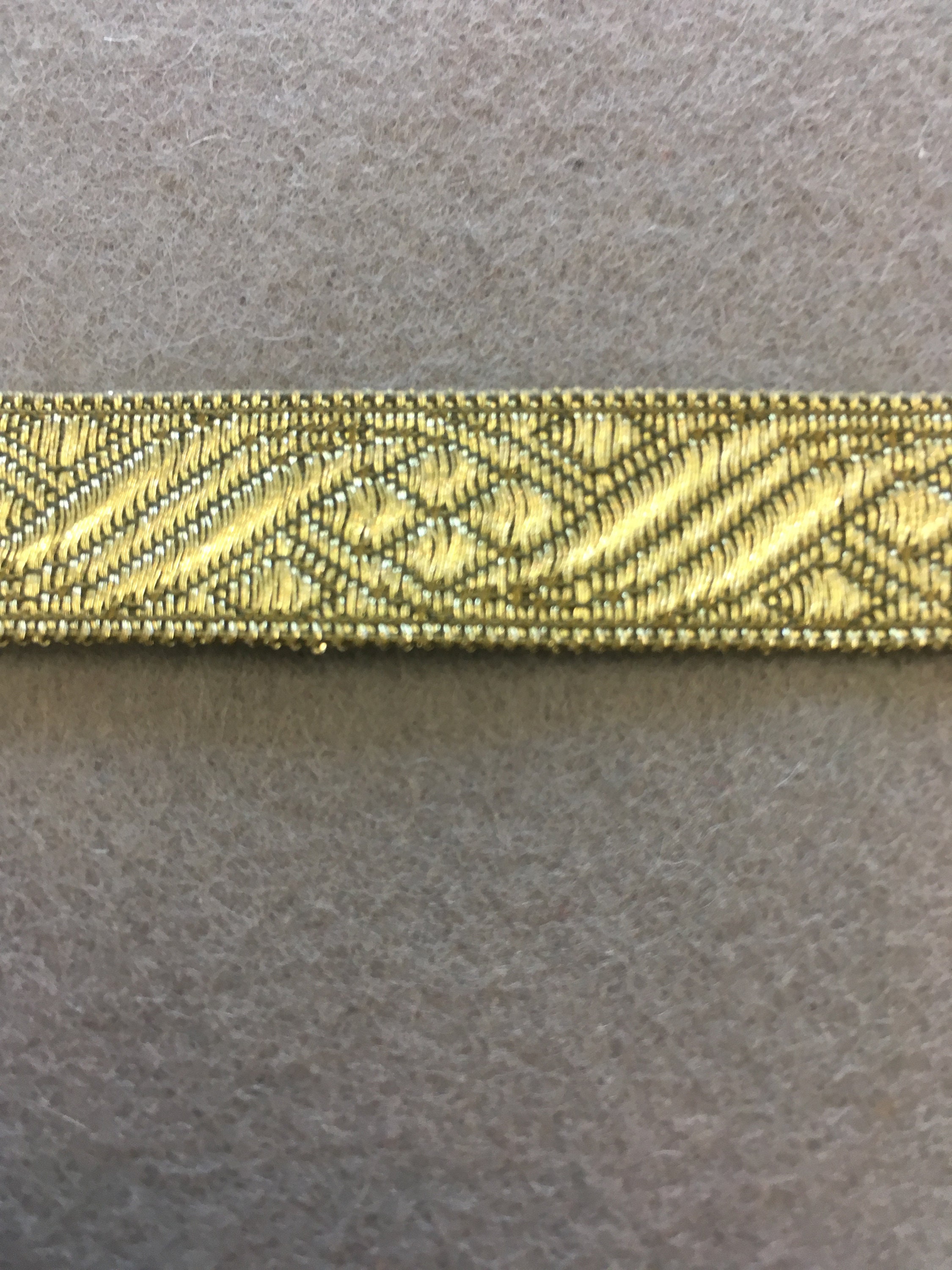 Patterned antique gold flat trim with two straight edges. 13/16 wide