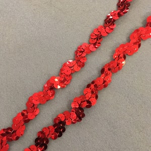 May include: Red sequin trim with a wavy pattern. The trim is made of small, round sequins that are sewn together in a continuous line.