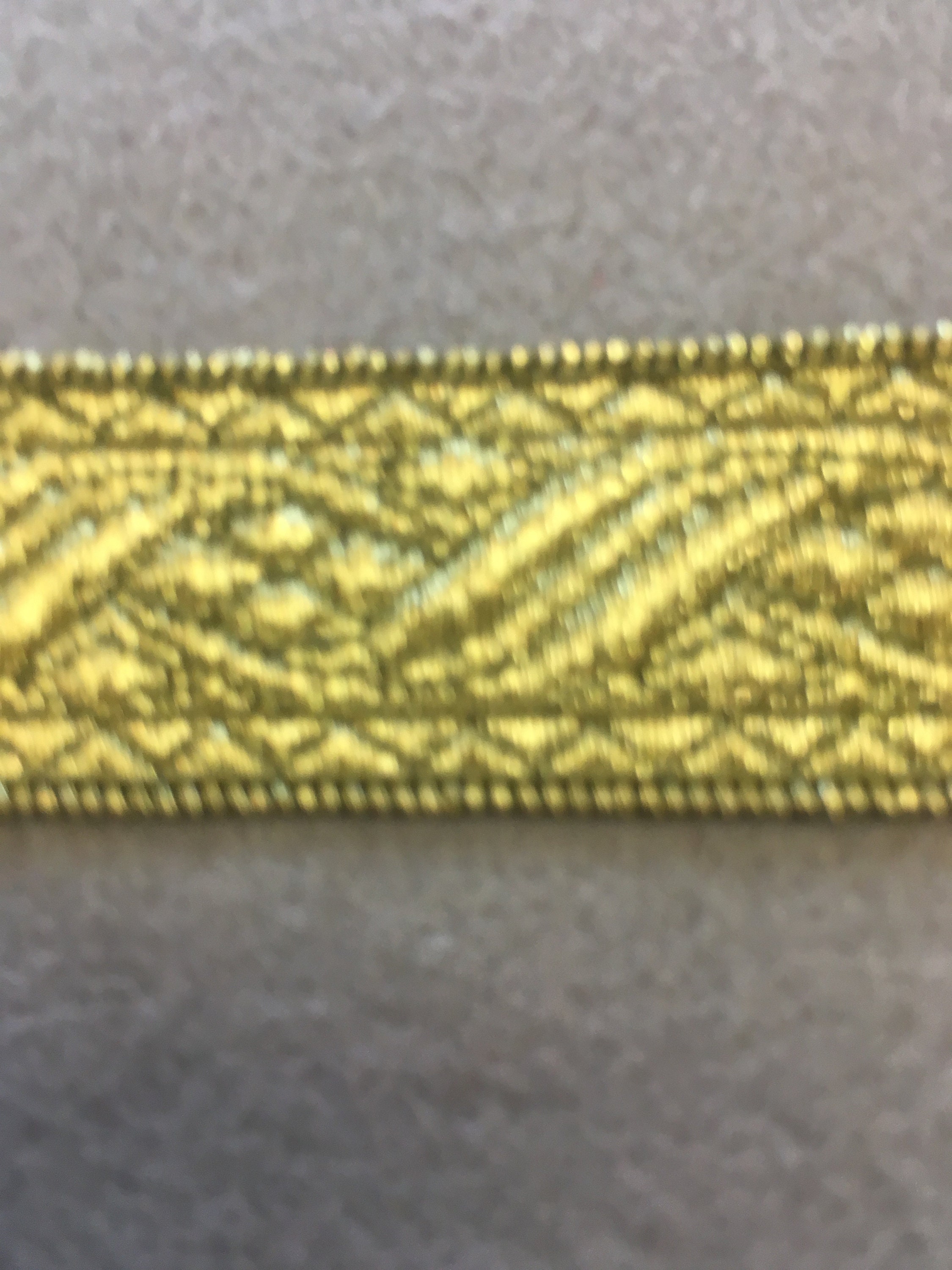 Patterned antique gold flat trim with two straight edges. 13/16 wide