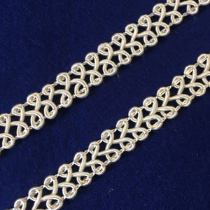May include: Two pieces of ivory-colored trim with a woven, interlaced design. The trim has a delicate, intricate pattern.