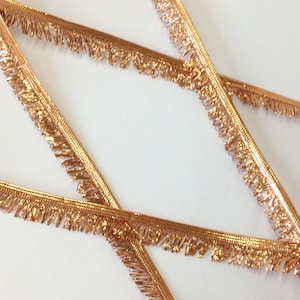 May include: Rose gold fringe trim with a metallic sheen. The fringe is approximately 1/2 inch wide.