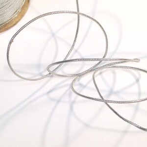 May include: A silver metallic cord with a textured surface. The cord is coiled and ready to be used for crafting or decorating.