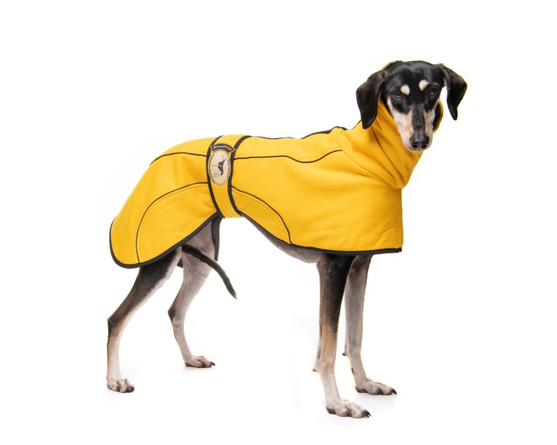 May include: A black and tan dog wearing a yellow fleece dog coat with black trim. The coat has a small patch on the back with a dog silhouette.