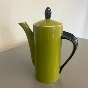 May include: A green ceramic teapot with a black handle and lid. The lid has a black knob on top.