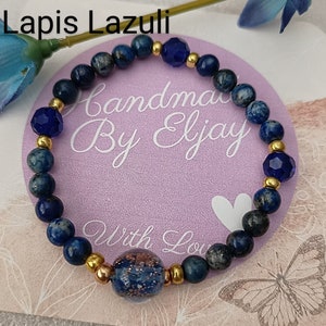 May include: A lapis lazuli beaded bracelet with gold spacers and a large lapis lazuli bead in the centre. The bracelet is on a pink background with the text "Handmade By Eljay With Love".