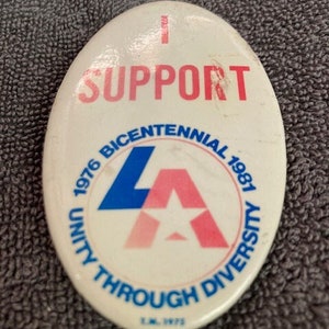May include: A white button with blue and pink lettering that reads "I Support Unity Through Diversity 1976 Bicentennial 1981 LA".