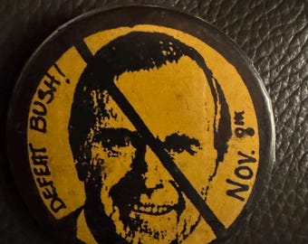 May include: A black and yellow button with a red slash through it. The button features a portrait of George H.W. Bush and the text "DEFEAT BUSH!" and "NOV. 8th".